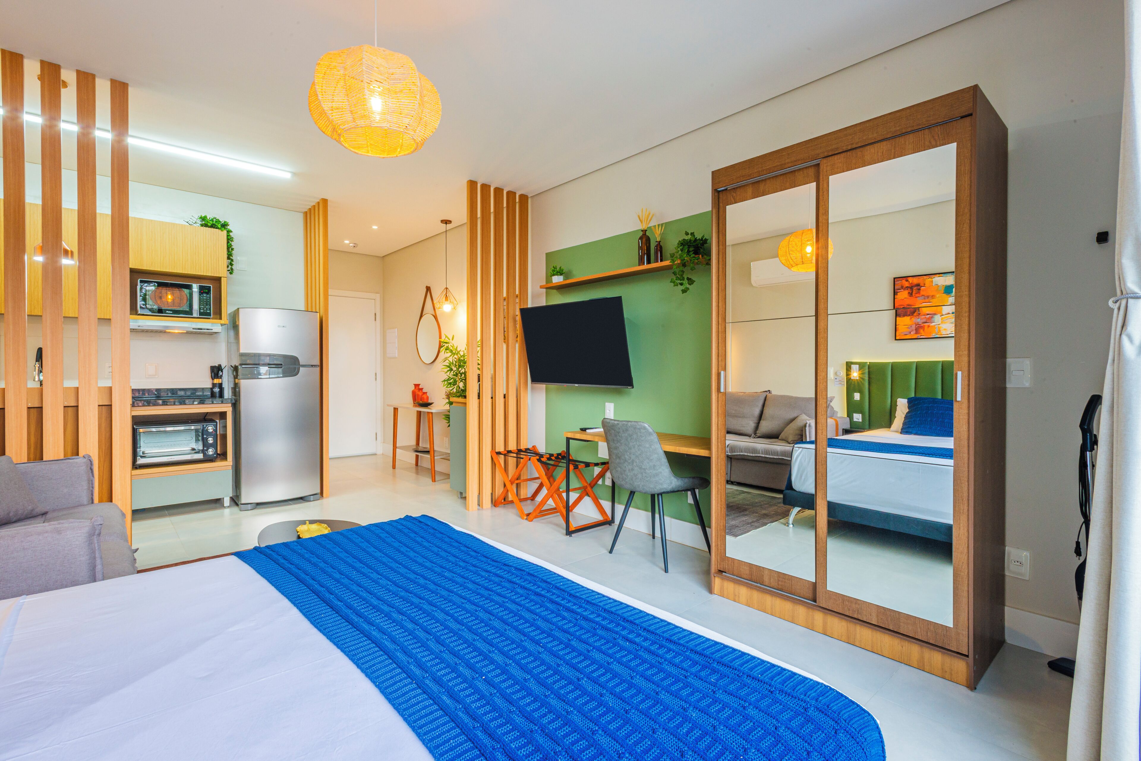 Une chambre d’hôtel moderne équipée d’un lit, d’un bureau, d’une chaise, d’une télévision et d’une kitchenette.