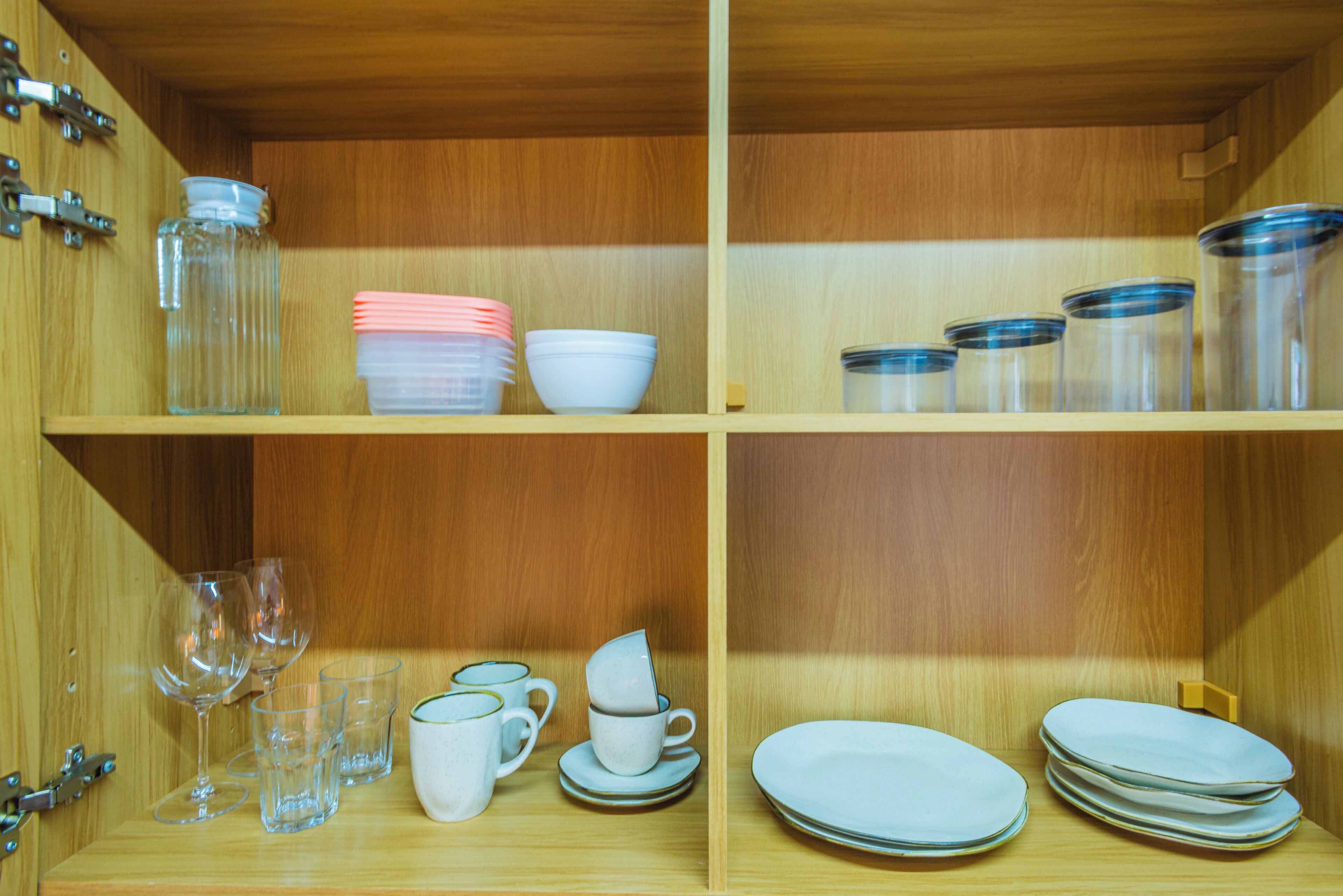 A wooden cabinet with shelves containing glass jars, plates, bowls, and cups.