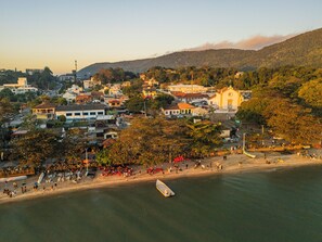 A coastal town with buildings, a beach, and a boat. - Studio Saint Garden - Sunset - Pool with Ocean View - Dining (Florianópolis)