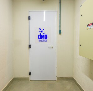 A white door with a logo and text indicating a shared laundry facility. - Studio Saint Garden - Sunset - Swimming pool with ocean view - Gastronomy (Florianópolis)