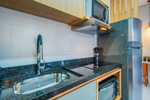 A modern kitchen with a stainless steel sink, a built-in microwave, and a stainless steel refrigerator. - Studio Saint Garden - Sunset - Pool with Ocean View - Dining (Florianópolis)