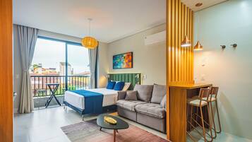 Quarto de hotel moderno com varanda, sofá, cama e área de refeições.