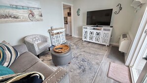 A living room with a sofa, ottoman, TV stand, and a painting. - Oceanfront Condo Newly Renovated (Hampton)