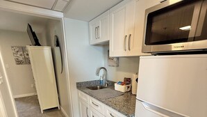 A compact kitchen with white cabinets, a microwave, a sink, and a refrigerator. - Oceanfront Condo Newly Renovated (Hampton)
