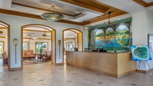 A spacious lobby with a reception desk, arched doorways, and a mural of a tropical landscape. - Spend Thanksgiving 2026 in Paradise! 2BR/2BA condo at The Point at Poipu (Koloa)