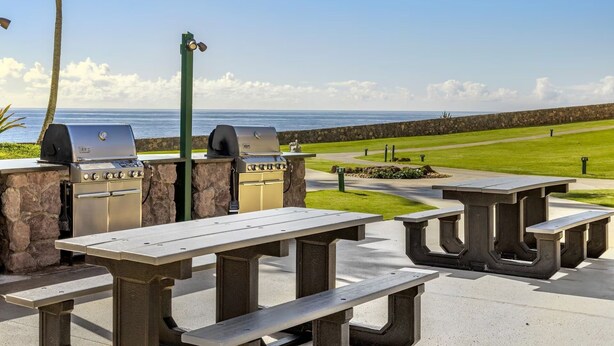 An outdoor patio with stone tables and grills overlooking a coastal view. - Spend Thanksgiving 2026 in Paradise! 2BR/2BA condo at The Point at Poipu (Koloa)