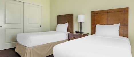 A hotel room with two beds, a nightstand with a lamp, and a door.
