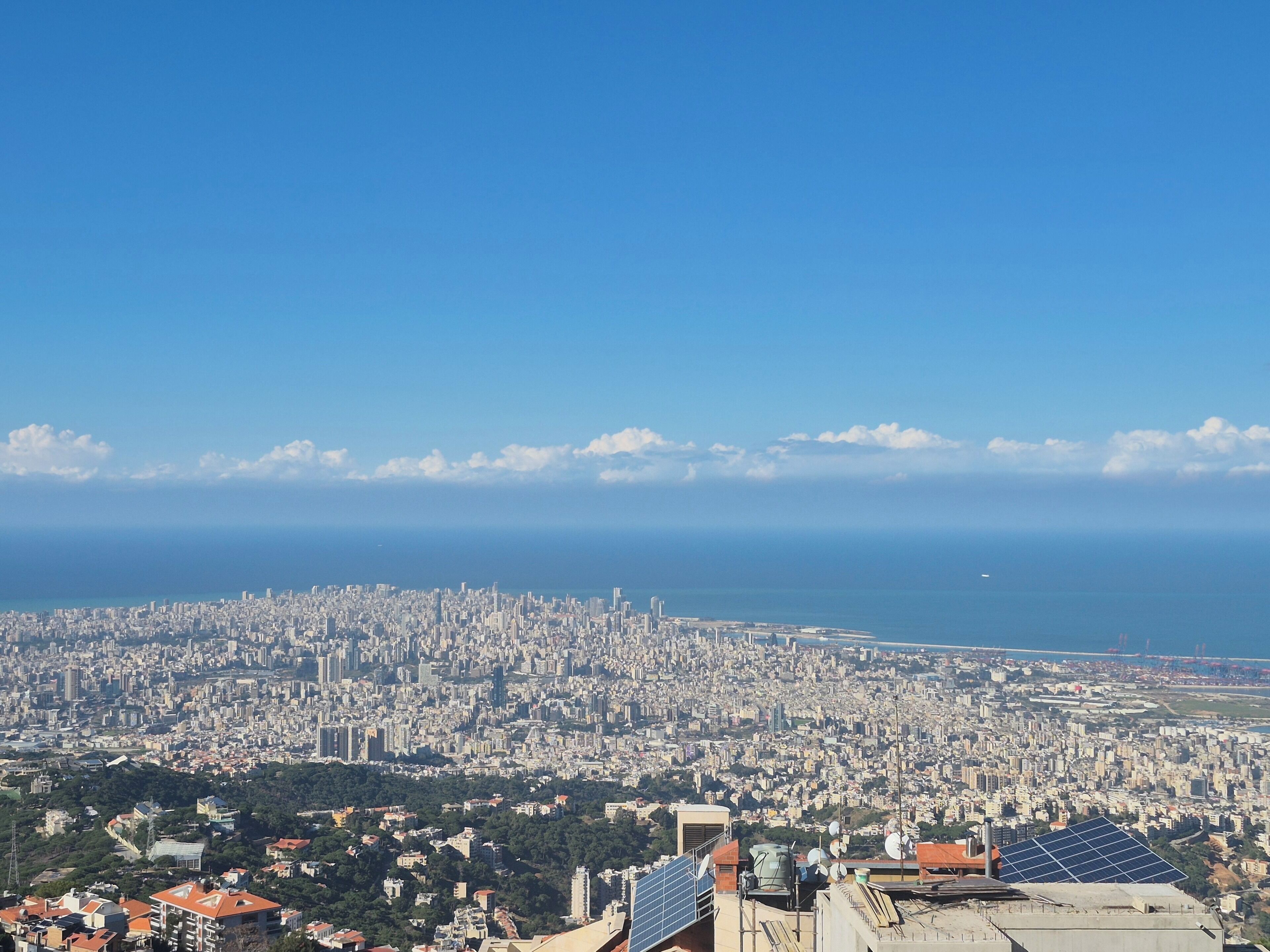 A cityscape with a view of the sea, numerous buildings, and a clear sky.