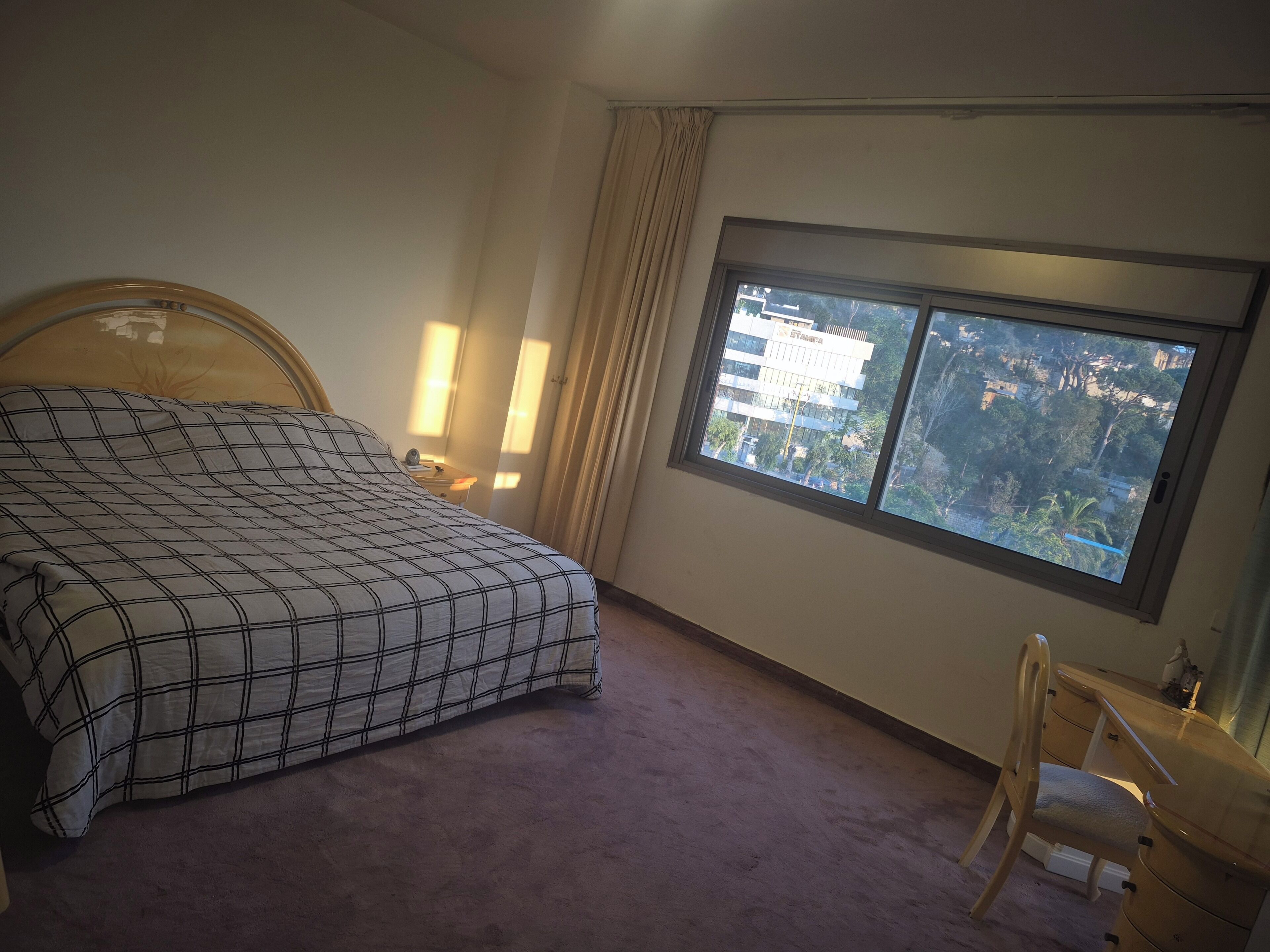 Un dormitorio con cama, escritorio, silla y ventana que ofrece vistas a edificios, además de una cortina.