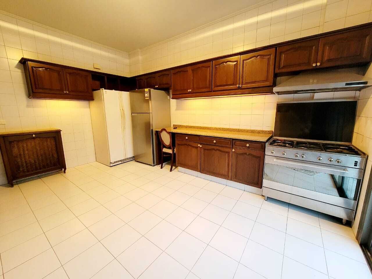 A kitchen with wooden cabinets, a refrigerator, a stove, and a chair.