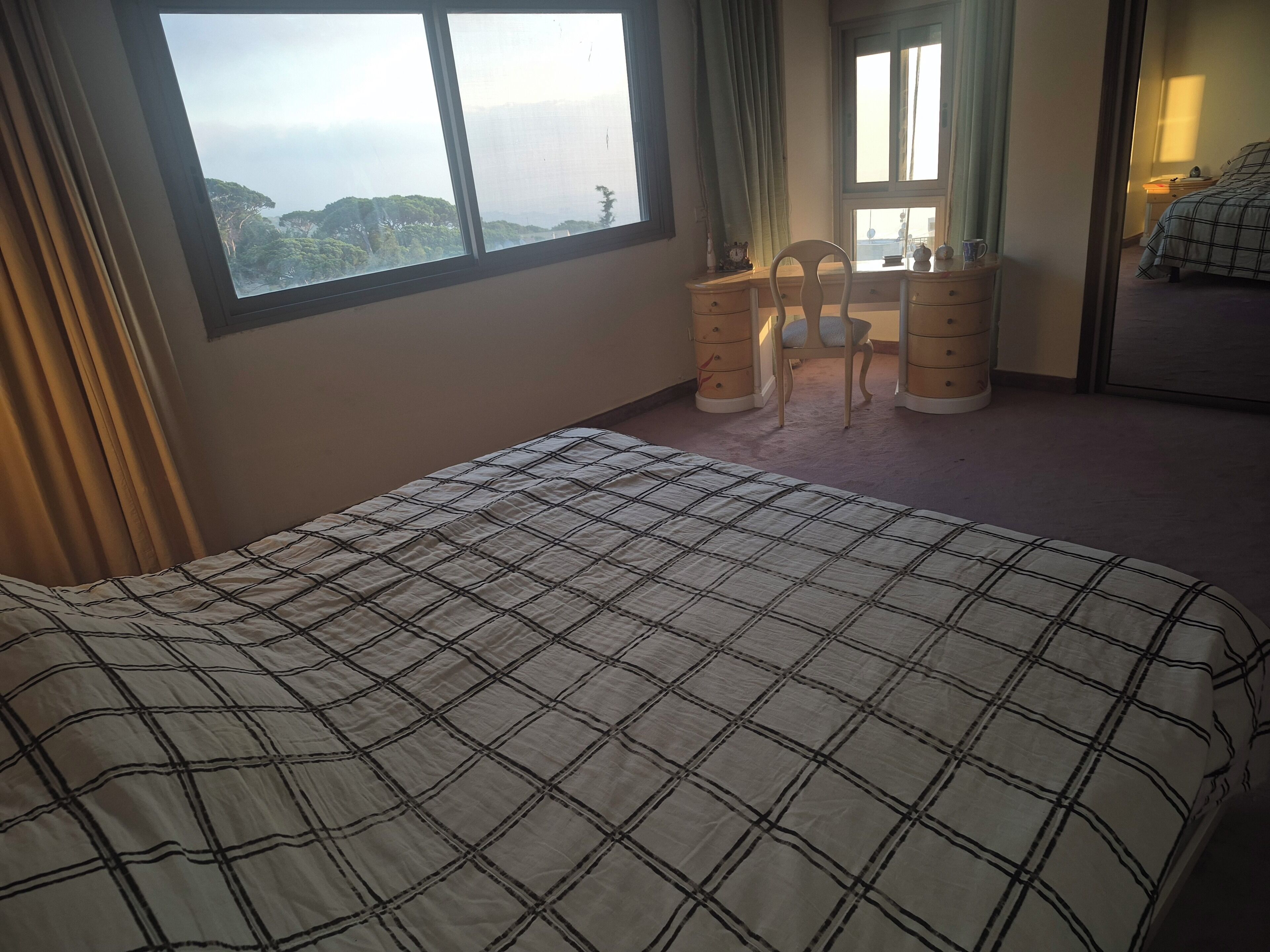 A hotel room with a large bed, a dresser, and a window with a view of the mountains.