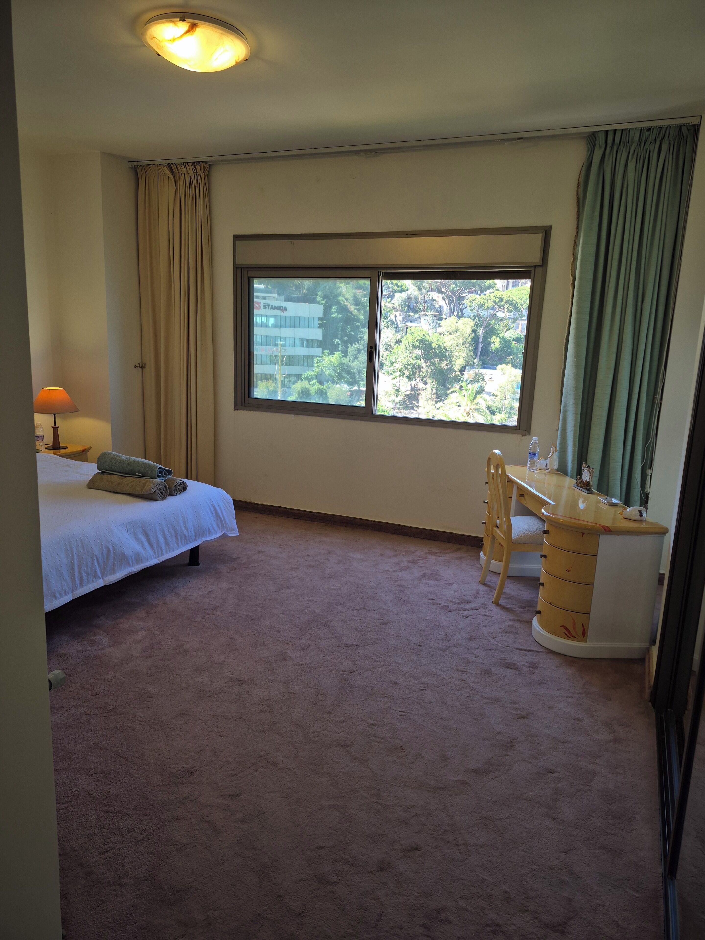 Une chambre d’hôtel avec un lit, un bureau, une chaise, une fenêtre et une lampe.