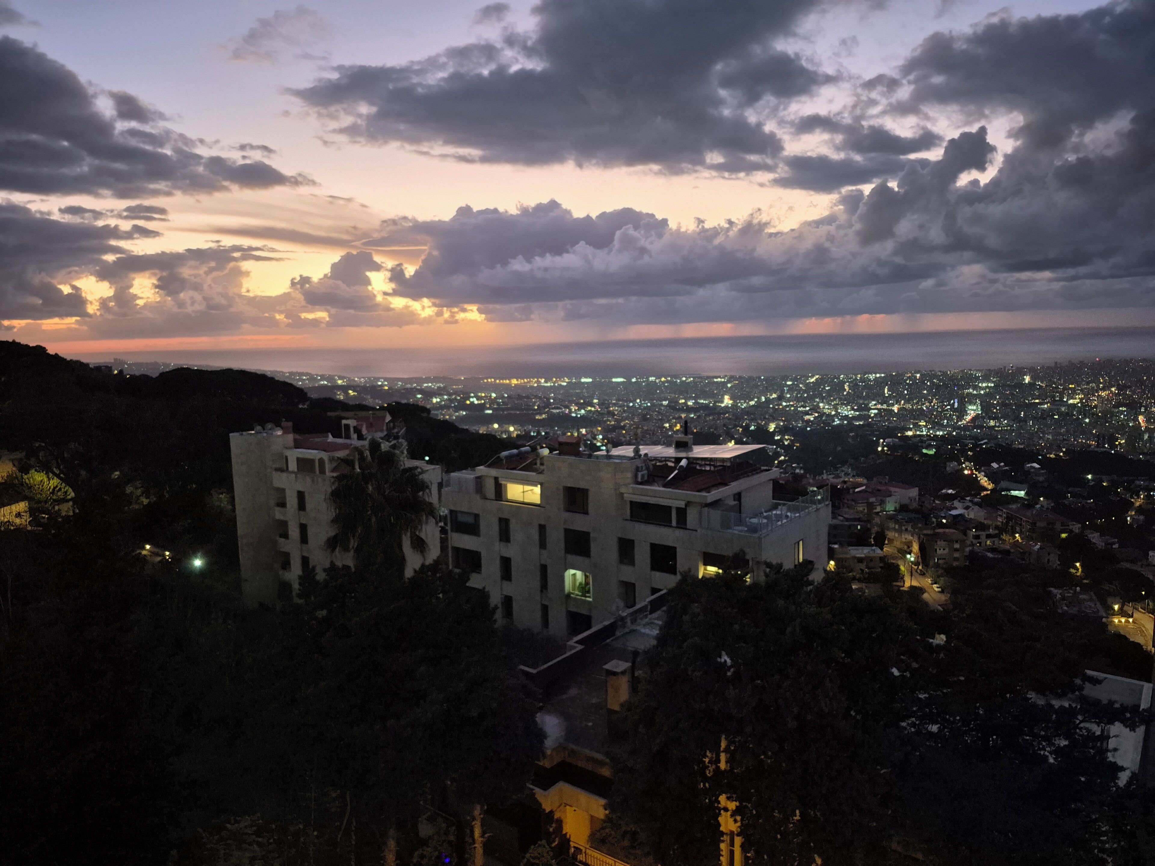 A cityscape at dusk with buildings and a view of the city lights.