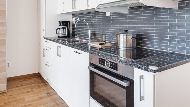 Cocina compacta con armarios blancos, salpicadero de baldosas negras, horno Bosch y cafetera.