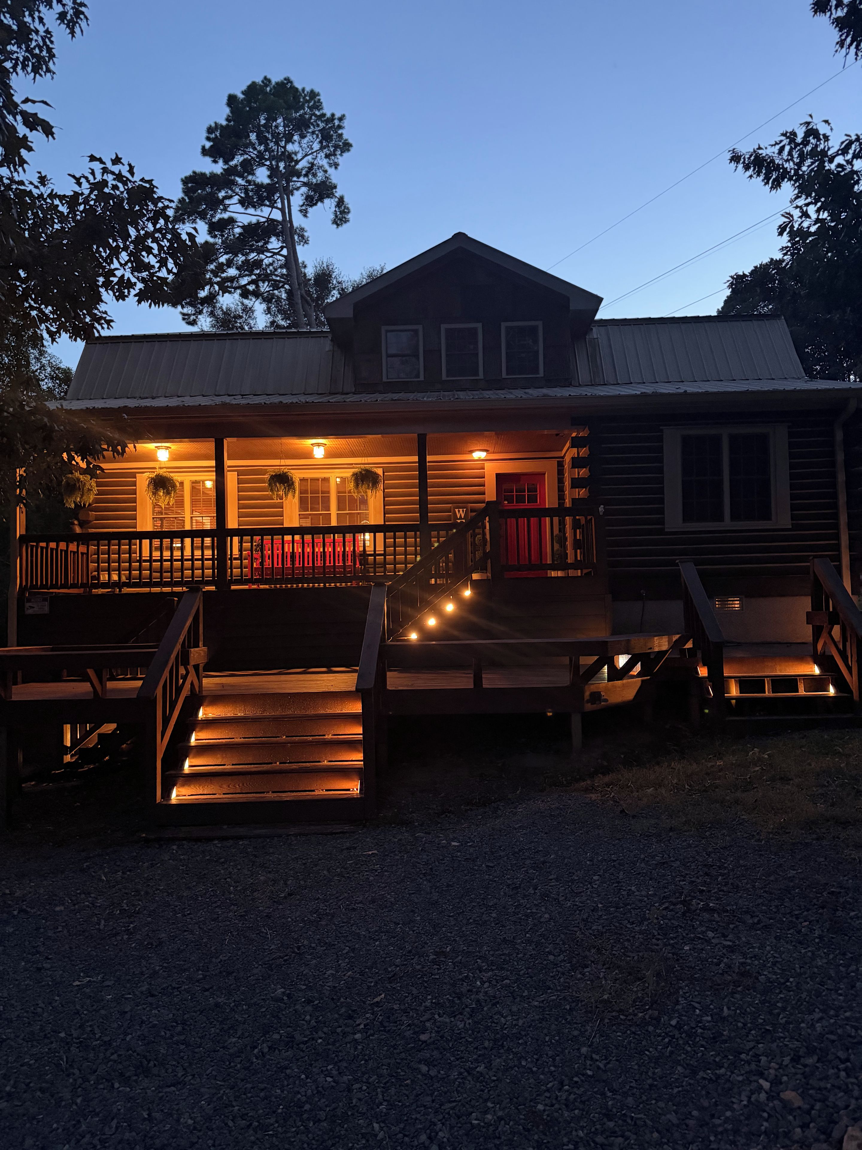 A two-story log cabin with a porch, wooden steps, and a red door.