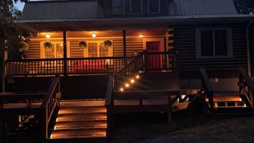 A two-story log cabin with a porch, wooden steps, and a red door.