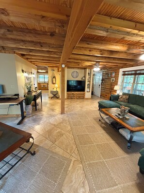 A spacious living area with a wooden ceiling, a large flat-screen TV, a green sofa, and a coffee table. - Welcome to Honey Hole Cabin located 1/2 mile from GTO Waterfront and boat ramp. (Scottsboro)