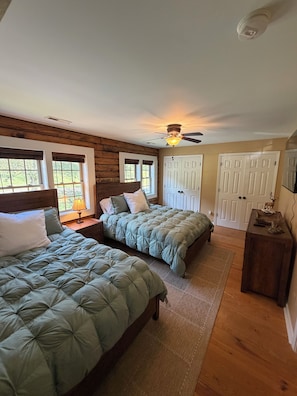 A bedroom with two beds, wooden walls, a ceiling fan, and a view of the outdoors.