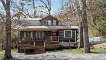 A rustic cabin with a porch, wooden deck, and a small staircase leading to the entrance.