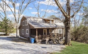 A wooden cabin with a porch, a staircase, and a gravel driveway.