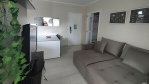 Una sala de estar con un sofá, un televisor y un refrigerador. Hay una puerta que da a otra habitación.
