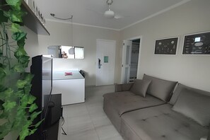 Una sala de estar con un sofá, un televisor y un refrigerador. Hay una puerta que da a otra habitación.