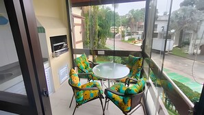Un balcón con una mesa y sillas de vidrio, un televisor y vistas a una zona residencial.