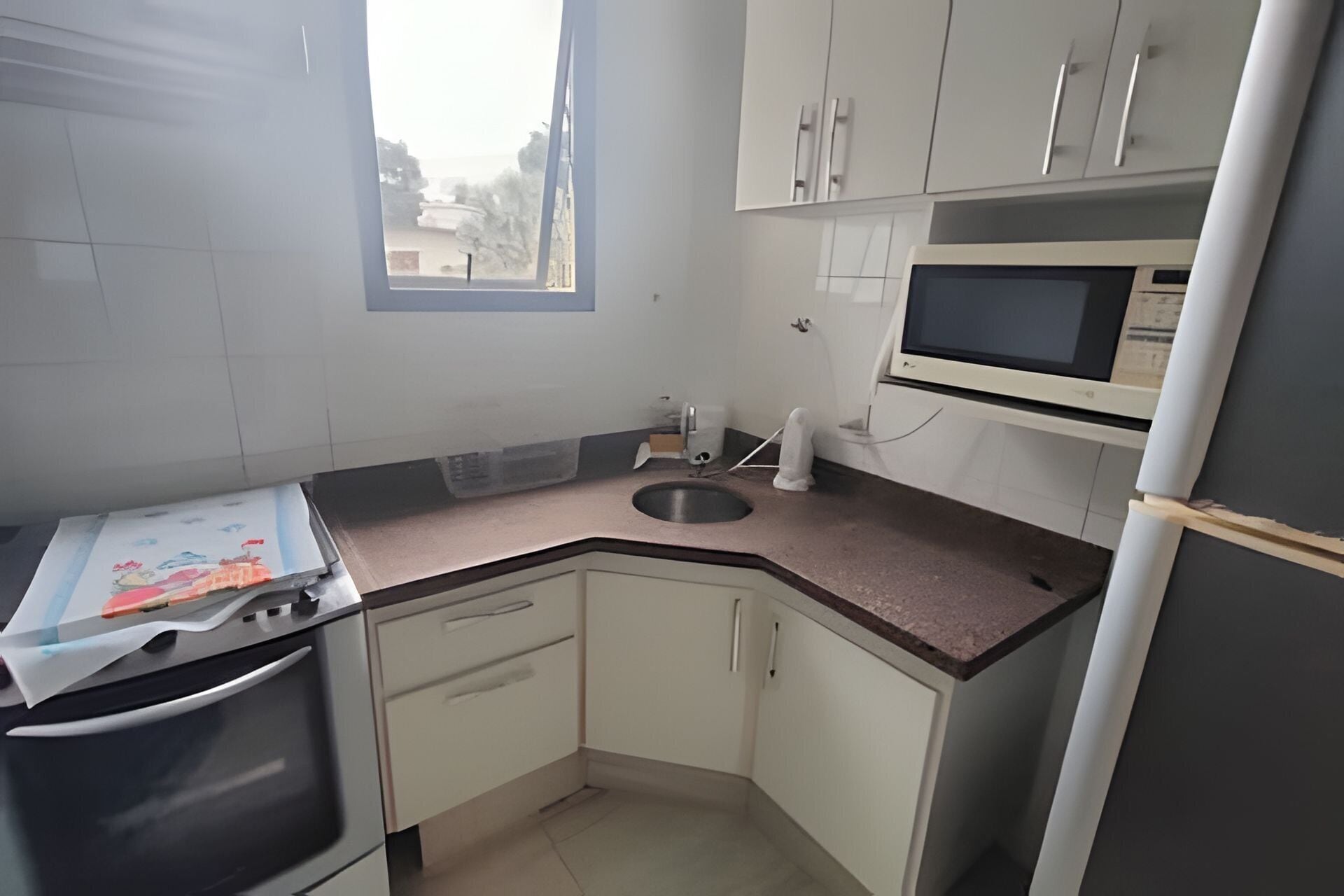 A compact kitchen with white cabinets, a microwave, a sink, and a stove.