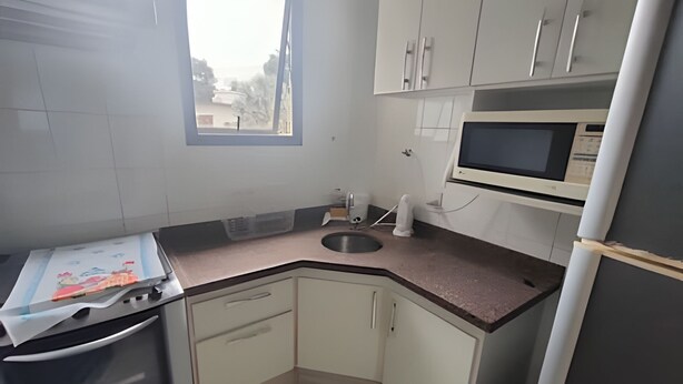 A compact kitchen with white cabinets, a microwave, a sink, and a stove. - SHB Riviera Dreams com Piscina e Sauna  (Bertioga)