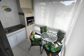Una cocina compacta con un lavamanos, una pequeña encimera y una ventana con cortinas. Frente a la ventana, hay una mesa con sillas.