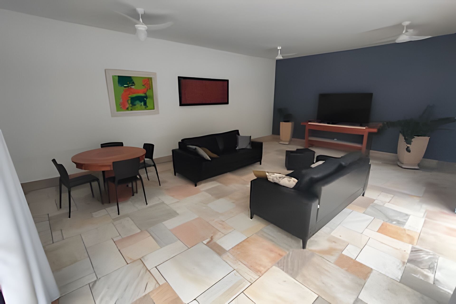 Una sala de estar moderna con una mesa redonda de madera, dos sofás negros, un televisor y un ventilador de techo.