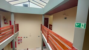 A multi-level interior with a central staircase, fire safety equipment, and emergency exit signage. - SHB Riviera Dreams com Piscina e Sauna  (Bertioga)