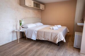 A single bed with a white bedspread and pillows, a small bedside table with a vase of flowers, and a built-in cabinet above the bed.