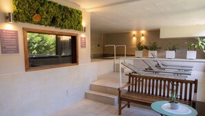 A hotel lobby with a reception desk, a wooden bench, a small table with a potted plant, and a wall-mounted green wall. - real village roma (Roma)