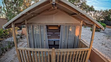 Eine kleine Holzhütte mit geneigtem Dach und einem Balkon, umgeben von Kies und Bäumen.