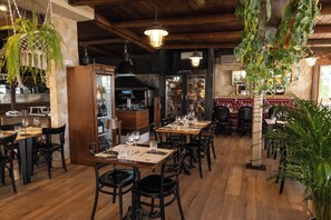 A restaurant interior with wooden floors, tables set with wine glasses, and hanging plants.