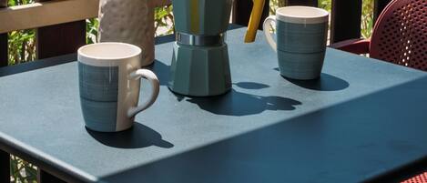 Una mesa con cafetera, taza y un florero con flores.