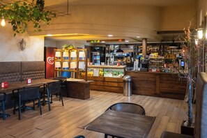 Interior de un restaurante con mesas y sillas de madera, una barra con una máquina de café y una vitrina con alimentos.
