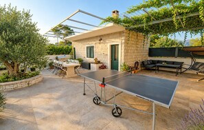 An outdoor patio with a ping pong table, seating area, and a stone building with a door. - Gorgeous home in Selca with WiFi (Selca)