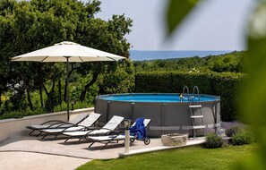 Ein Schwimmbecken mit Liegestühlen und einem Sonnenschirm, umgeben von viel Grün und freiem Blick auf die Landschaft.