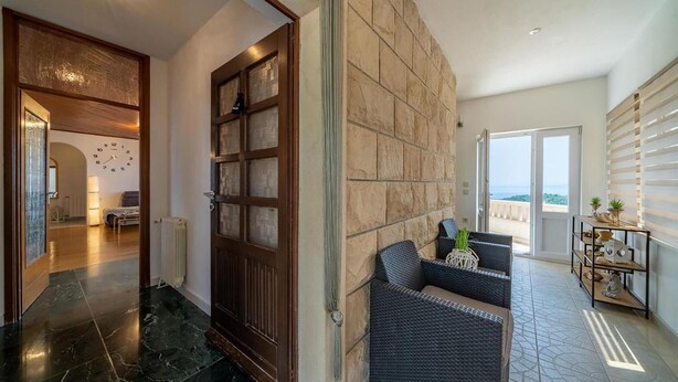 A modern interior with a stone wall, a dark wooden door, a wicker sofa, and a view of the sea through a sliding door. - Gorgeous home in Selca with WiFi (Selca)