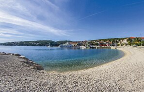 A pebbled beach with clear water, a dock with boats, and buildings in the background. - Gorgeous home in Selca with WiFi (Selca)