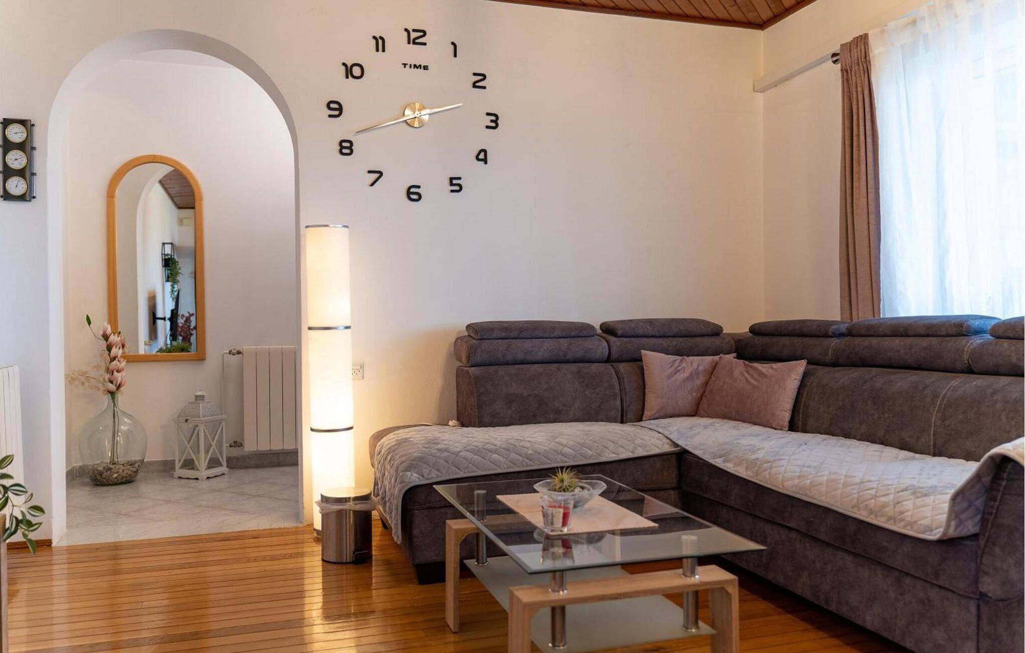 Uma sala de estar moderna com um sofá seccional, uma mesa de centro de vidro e um relógio de parede.