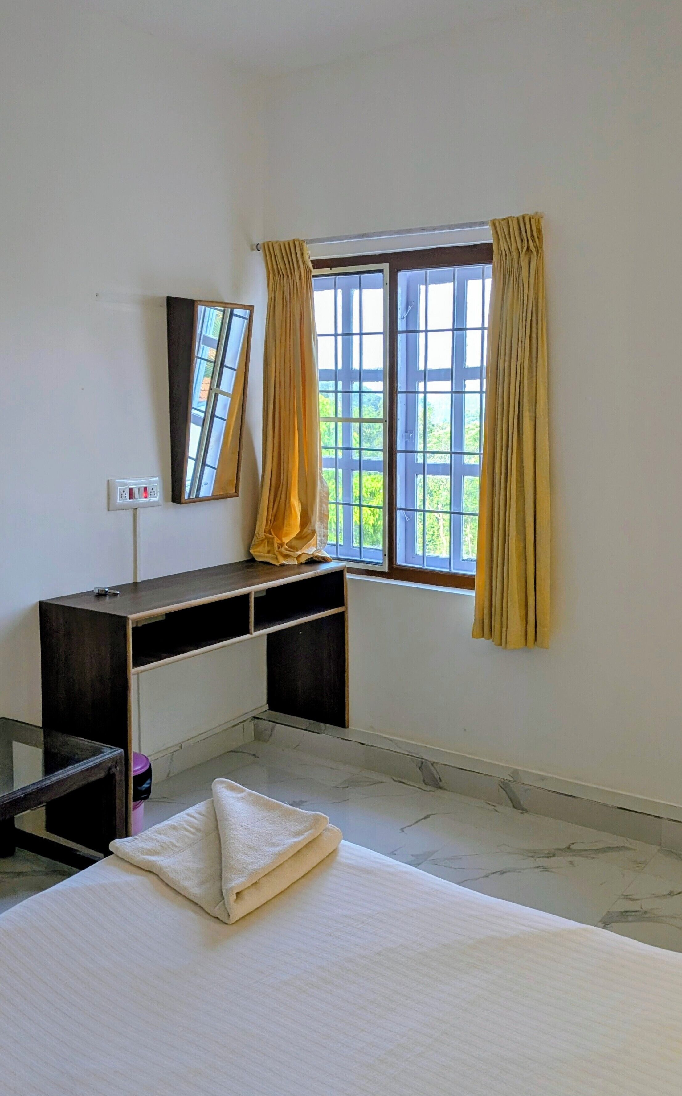 Una habitación con cama, escritorio, espejo y ventana con cortinas.