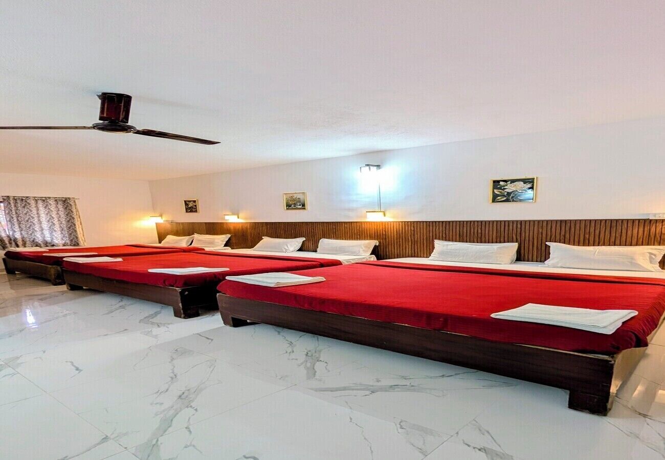 Habitación de hotel con cuatro camas, ventilador de techo, piso de mármol e iluminación montada en la pared.