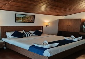 A double bed with a wooden headboard, a nightstand, a wardrobe, and a wall-mounted light fixture. - The Lantana Resort (Madikeri)