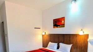 Habitación de hotel con una cama, ventilador de techo, luz de pared y un cuadro.
