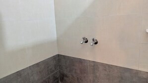 Un baño con azulejos blancos y grises, dos grifos empotrados en la pared y un desagüe en el suelo.