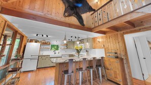 Una cocina con armarios de madera, una isla central con taburetes de bar y una decoración de oso colgante.