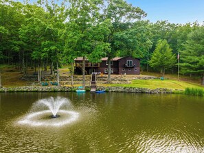 A lakeside cabin with a dock, a small boat, and a fountain. - Private Lake | 50 acres | Secluded Cabin | Hiking (Hawley)